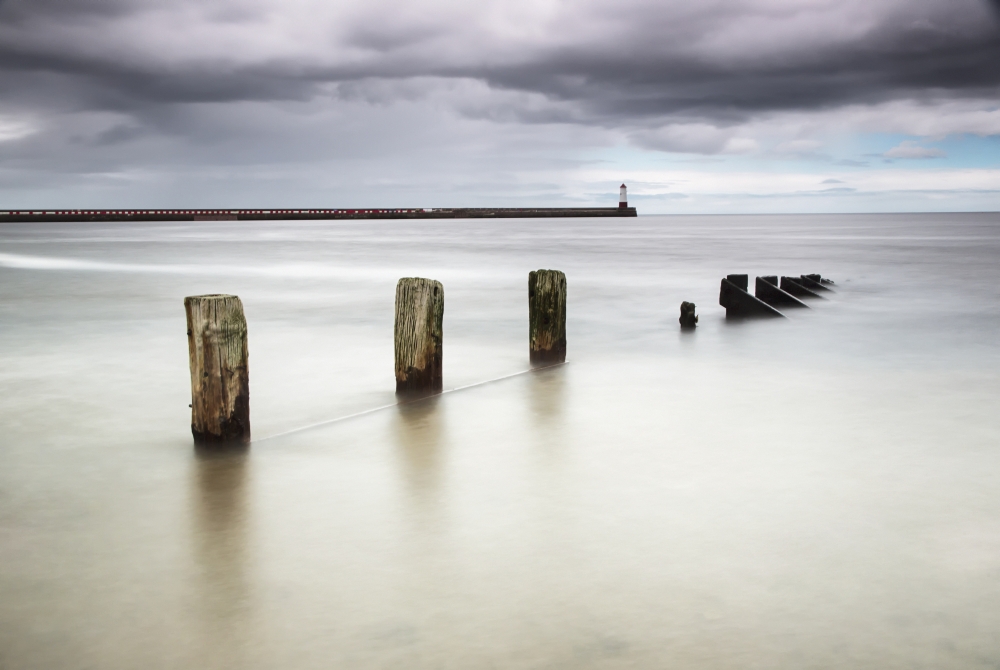 Dpi2114952 Wooden Posts In The Ocean With A Lighthouse At The End Of A Pier Poster Print, 18 X 12