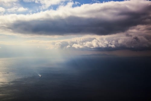 A Lone Boat On The Aegean Sea Under A Cloudy Sky & Distant View of The Coastline - Greece Poster Print by Reynold Mainse, 38 x 24 - Large