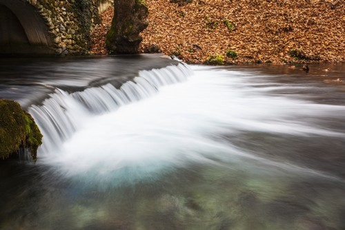 DPI12286705 Water Cascading Over A Ledge in a River with The Riverbank Covered with Autumn Poster Print by Reynold Mainse, 19 x 12