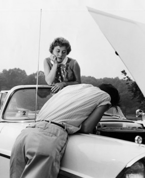 Rear View of a Young Man Examining His Car with a Young Woman Looking at Him Poster Print - 18 x 24 in.
