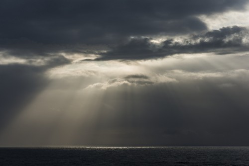 Sunlight Breaks Through The Clouds Over The Ocean On The Oregon Coast Cannon Poster Print by Robert L.Potts - 18 x 12