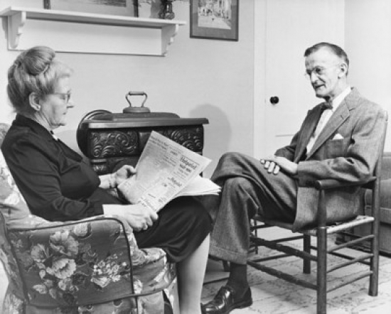 Senior Woman Reading a Newspaper with a Senior Man Sitting in Front of Her Poster Print - 18 x 24 in.