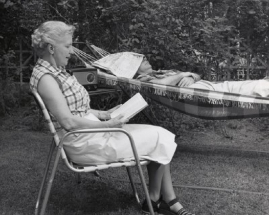 Side Profile of a Senior Woman Reading a Book with a Senior Man Sleeping in a Hammock Poster Print - 18 x 24 in.