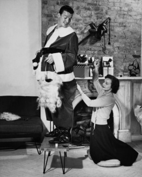 Side Profile of a Mid Adult Man Standing with a Mid Adult Woman Stitching His Costume Poster Print 18 x 24 in.