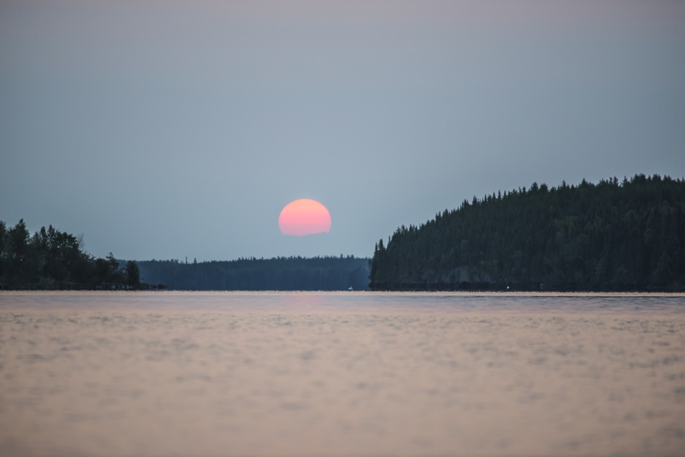 DPI12305745 A Red Sun Setting Over The Forest with A Lake Reflecting The Pink Glow - Manitoba Canada Poster Print by Thomas Fricke, 19 x 12