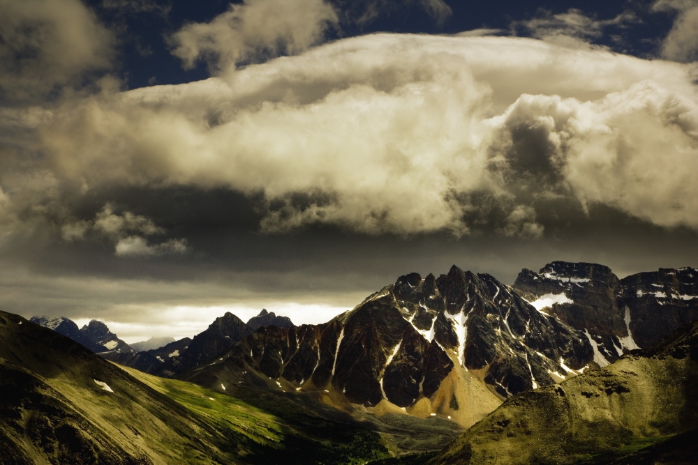 Patches of Light Find Their Way Through Hovering Clouds Above Mountain Range Poster Print by Darren Greenwood, 17 x 11