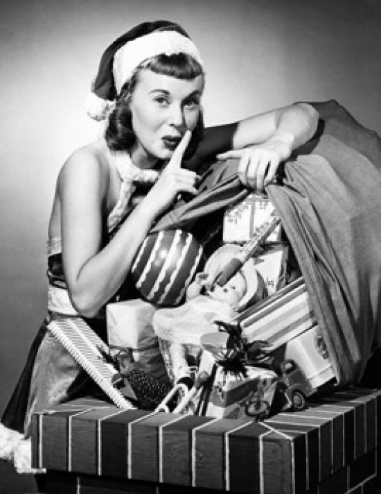 Portrait of a Young Woman Standing Near a Sack of Christmas Gifts with Her Finger on Her Lips Poster Print - 18 x 24 in.
