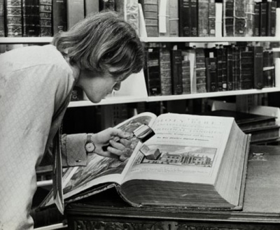 Young Man Examining a Miniature Bible in a Library Poster Print - 18 x 24 in.