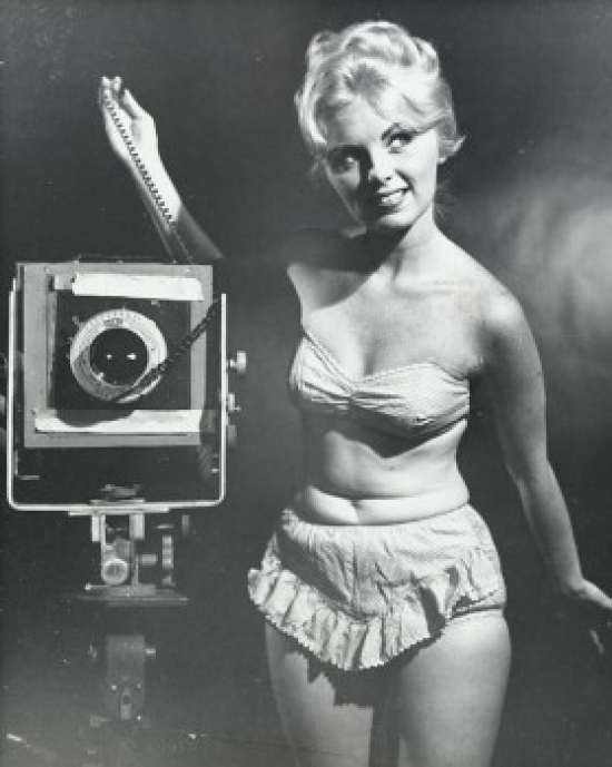 Young Woman Standing with a Camera Poster Print - 18 x 24 in.