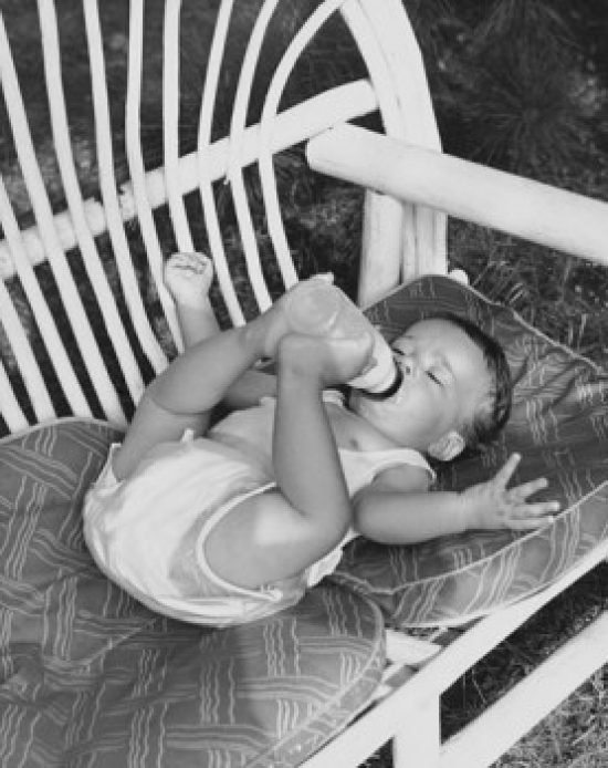 High Angle View of a Baby Lying on a Couch & Drinking Milk From a Bottle Poster Print - 18 x 24 in.