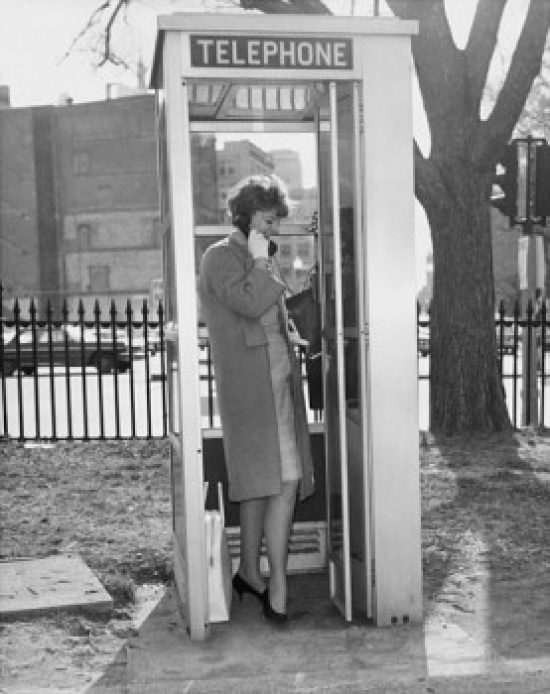 Side Profile of a Young Woman Talking on the Phone in a Telephone Booth Poster Print - 18 x 24 in.
