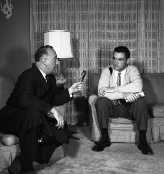 Two Men Talking in Living Room Poster Print - 18 x 24 in.