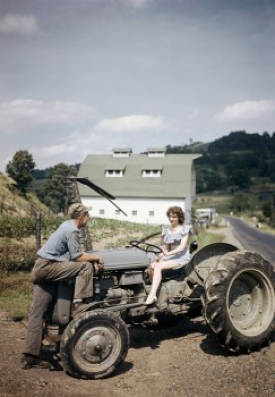Young Woman Sitting on a Tractor with a Young Man Standing in Front of Her Poster Print - 18 x 24 in.