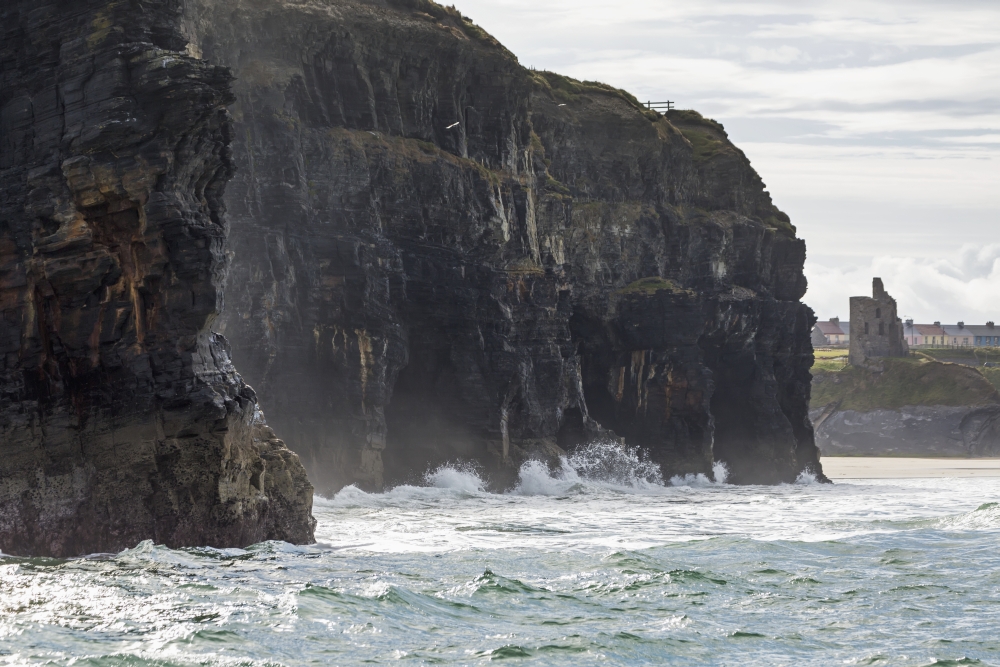 Dark Straight Cliffs with Waves Crashing Into The Rock with Ruined Castle Turret in Background - Ballybunion County Kerr Poster Print - 19 x 12 in.