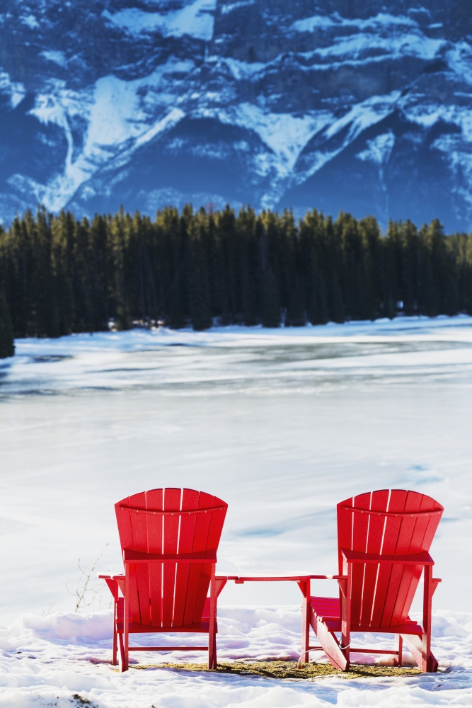 Two Red Chairs on Snow Covered Ridge Overlooking Frozen Lake with Snow Covered Mountain Cliff in The Background - Banff 1 Poster Print - 12 x 19 in.