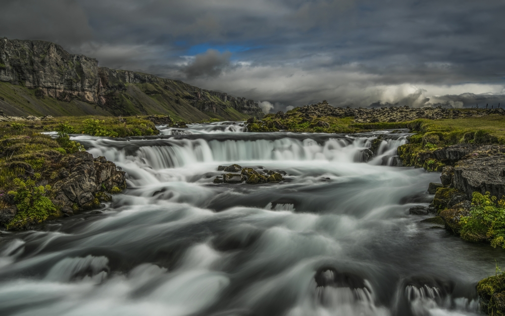 DPI12283202 Water Flowing Over A Rugged Landscape Under A Cloudy Sky - Iceland Poster Print - 19 x 12 in.