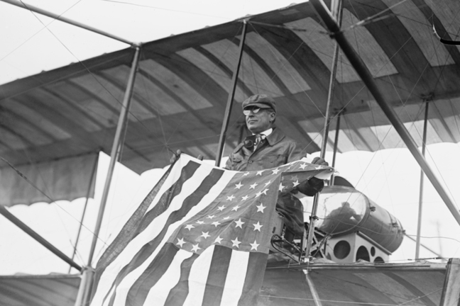 Picture of Buy Enlarge 0-587-46052-LP12x18 Aviator C.B. Harmon Unfurls Stars and Stripes from his pilot seat on his Biplane.- Paper Size P12x18
